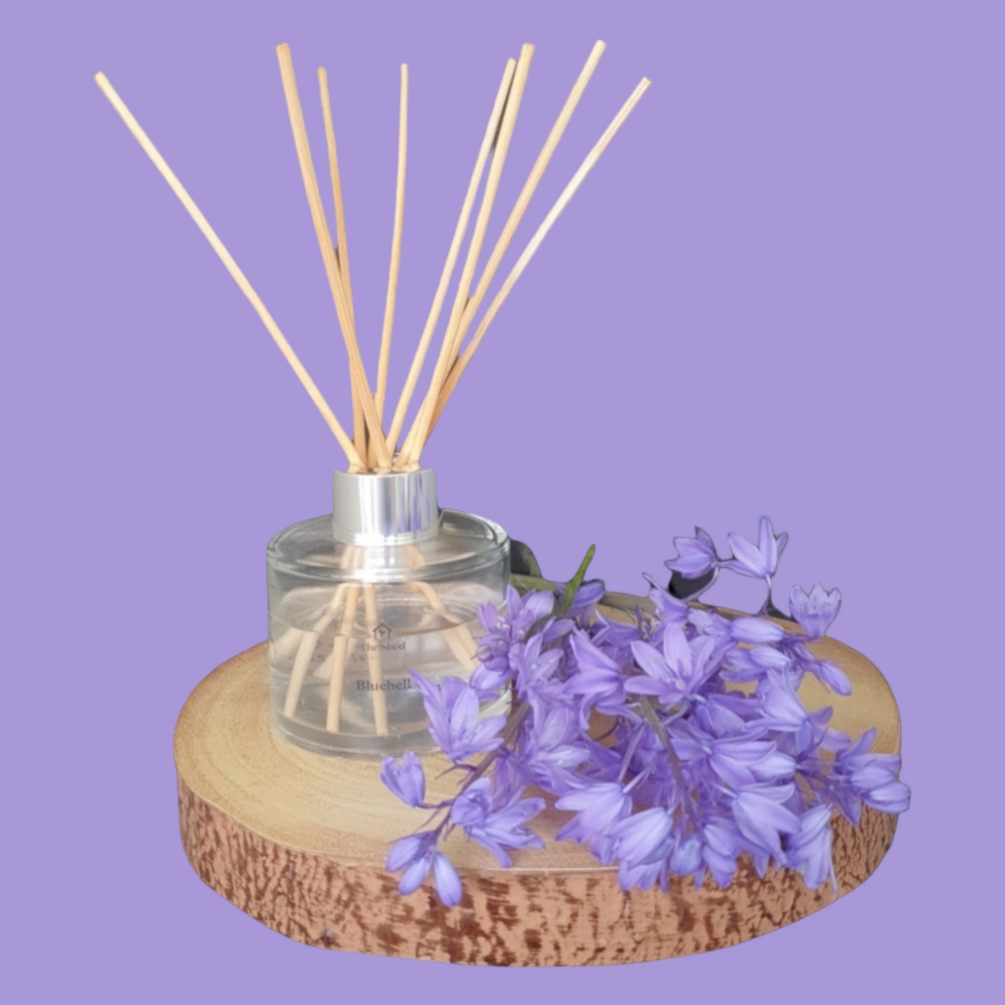 Picture shows The Shed Collection's vegan friendly Bluebell reed diffuser in a clear glass bottle with silver lid
7 reeds sitting on a log slice surrounded by a bunch of Bluebells freshly picked from their Bristol garden.