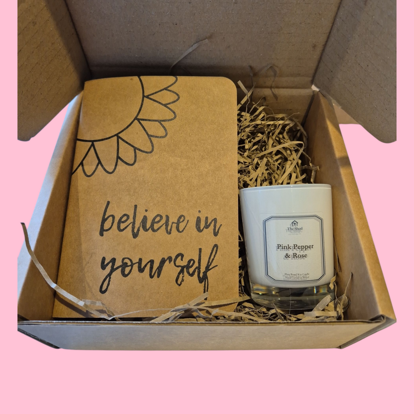 Gift set with a candle and a card that says 'believe in yourself' in a box on a pink background.