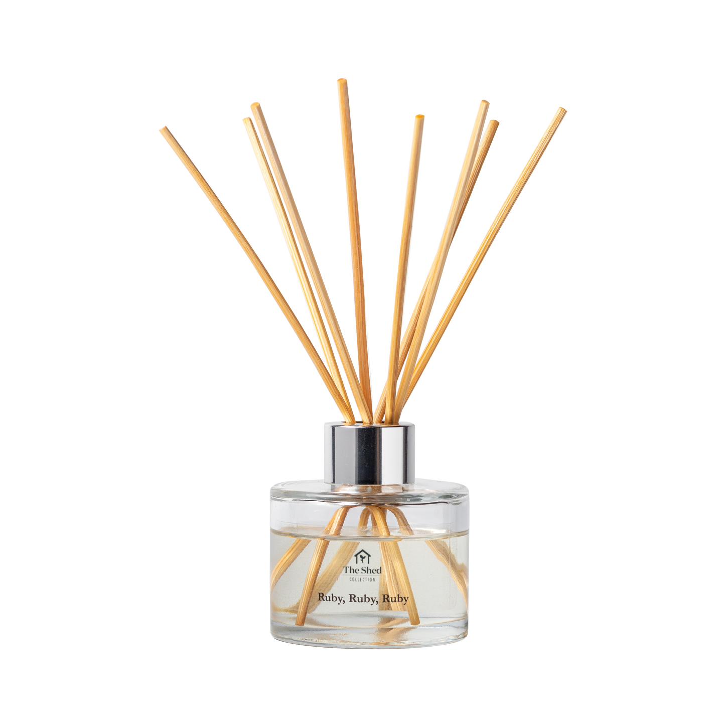 A reed diffuser bottle with a clear glass base, silver collar, and light natural reeds, labelled 'The Shed Collection' and 'Ruby, Ruby, Ruby'.