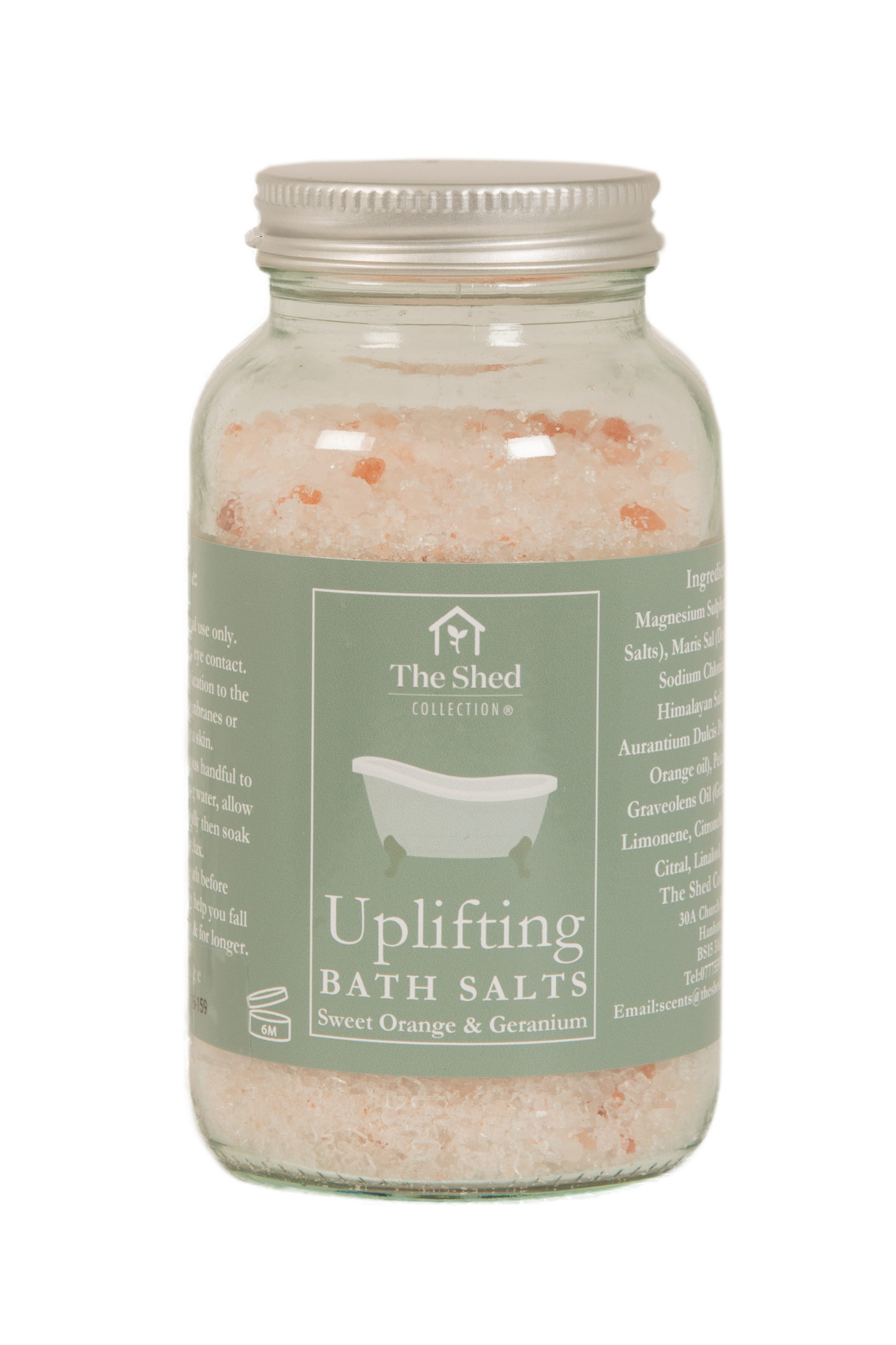 A glass jar of 'Uplifting Bath Salts' by The Shed Collection, filled with pink and orange crystalline bath salts, featuring a sage green label and a silver metal lid.