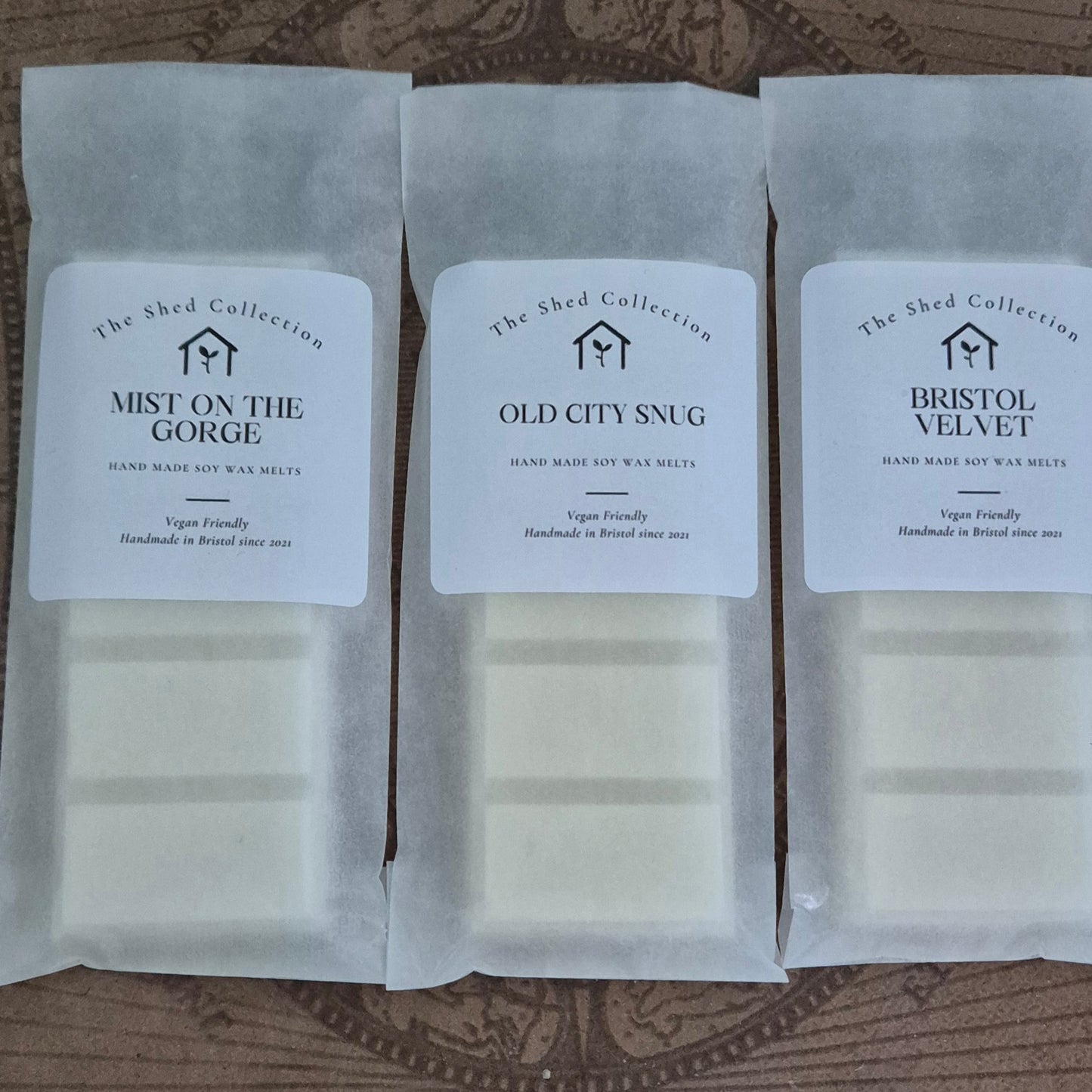 Three packages of 'The Shed Collection' wax melts on a wooden surface.