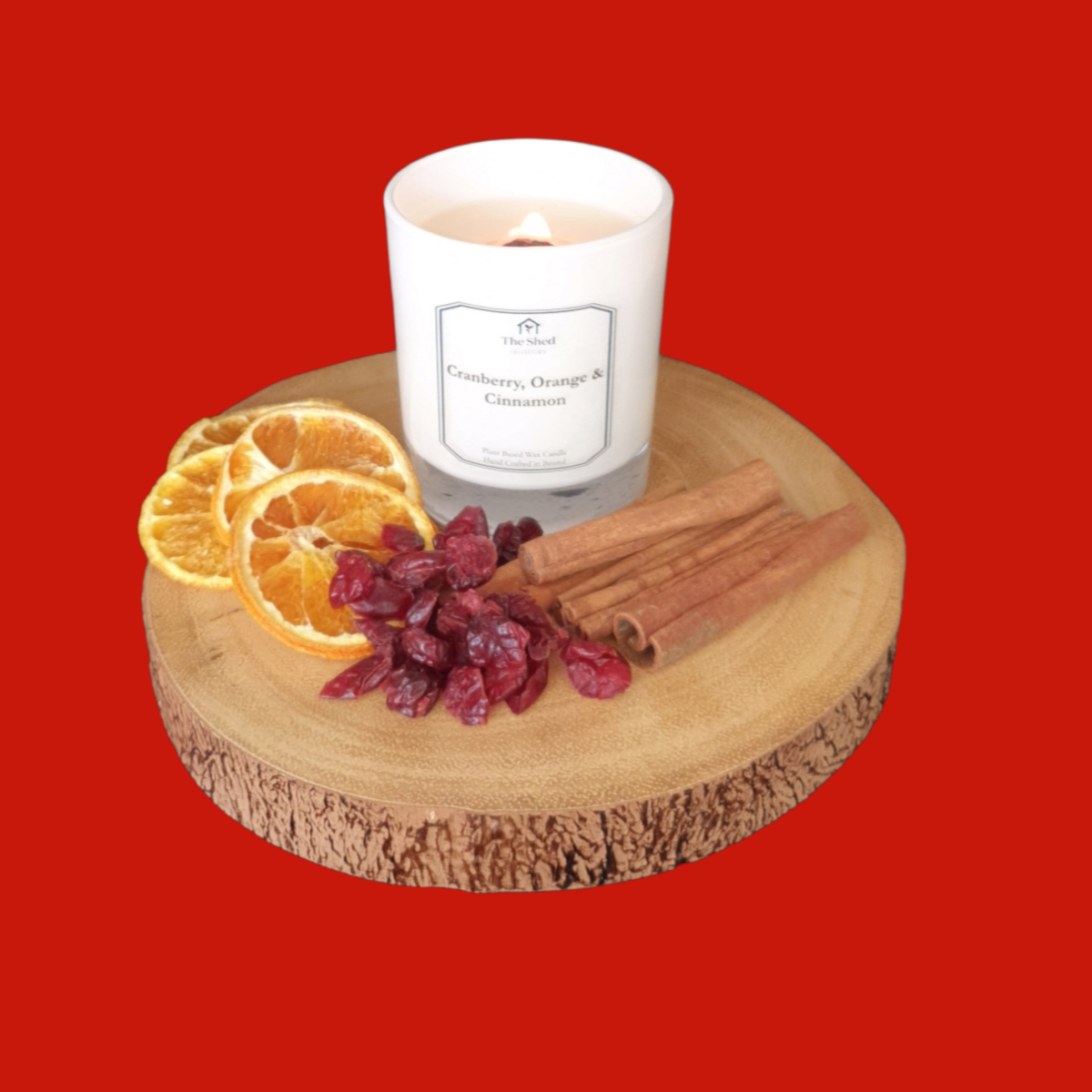 Candle with cranberry, orange, and cinnamon on a wooden coaster against a red background