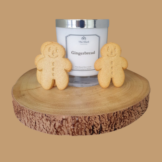 A candle with gingerbread label, placed on a wooden disc, with two actual gingerbread cookies on either side of the candle.