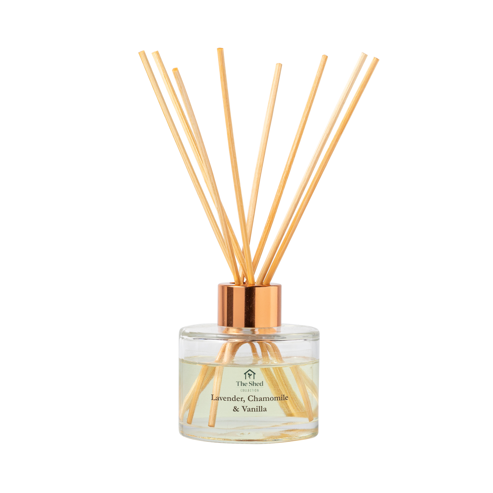 A reed diffuser bottle with a clear glass base, pale yellow liquid, cap and natural reeds, labeled 'The Shed Collection Lavender, Chamomile & Vanilla'.