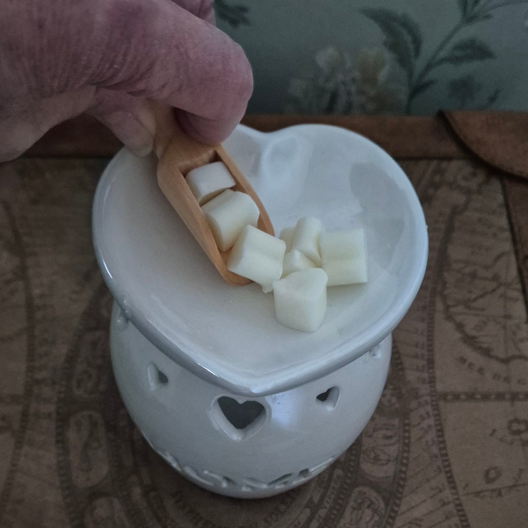 White ceramic warmer with heart designs on a floral-patterned fabric background