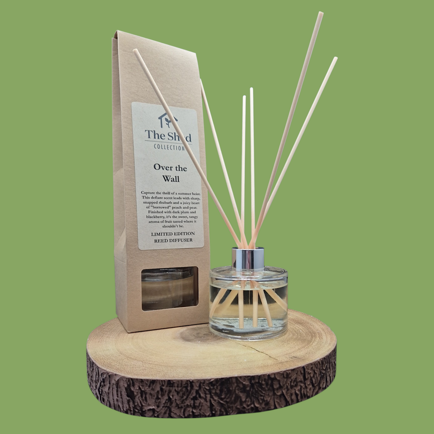 Reed diffuser set with packaging on a wooden stand against a green background