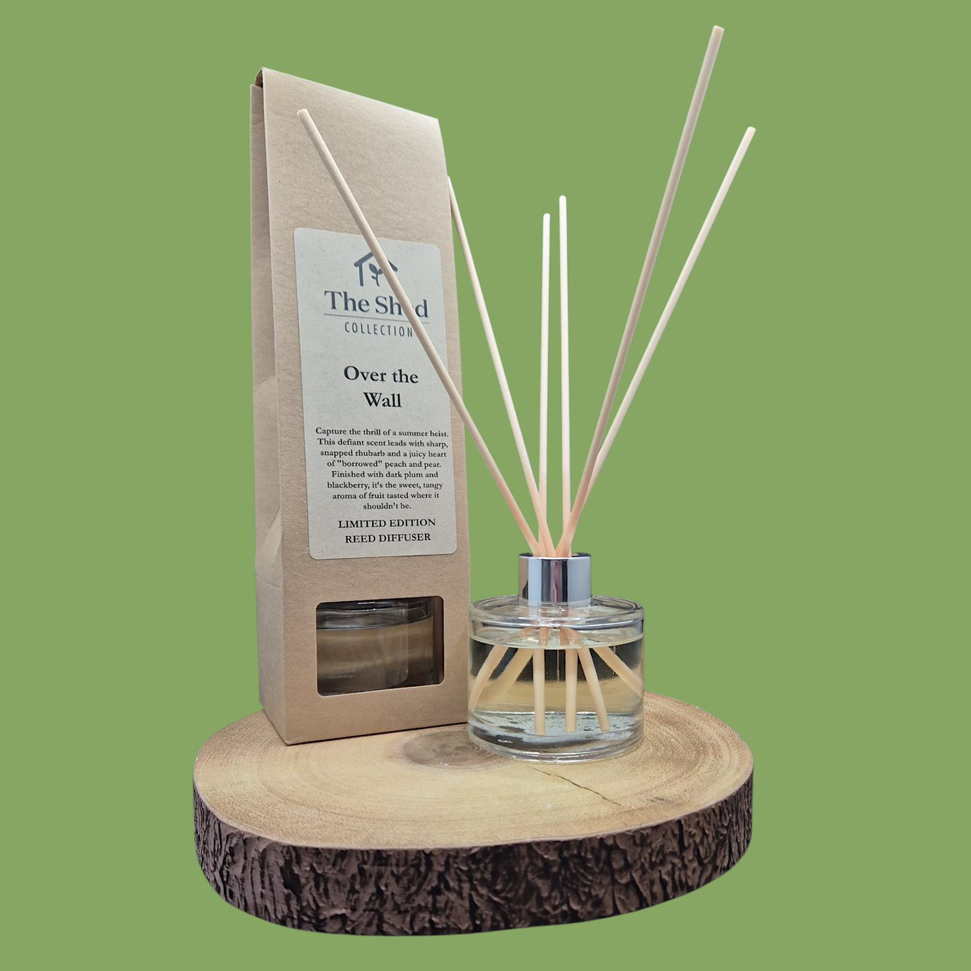Reed diffuser set with packaging on a wooden stand against a green background