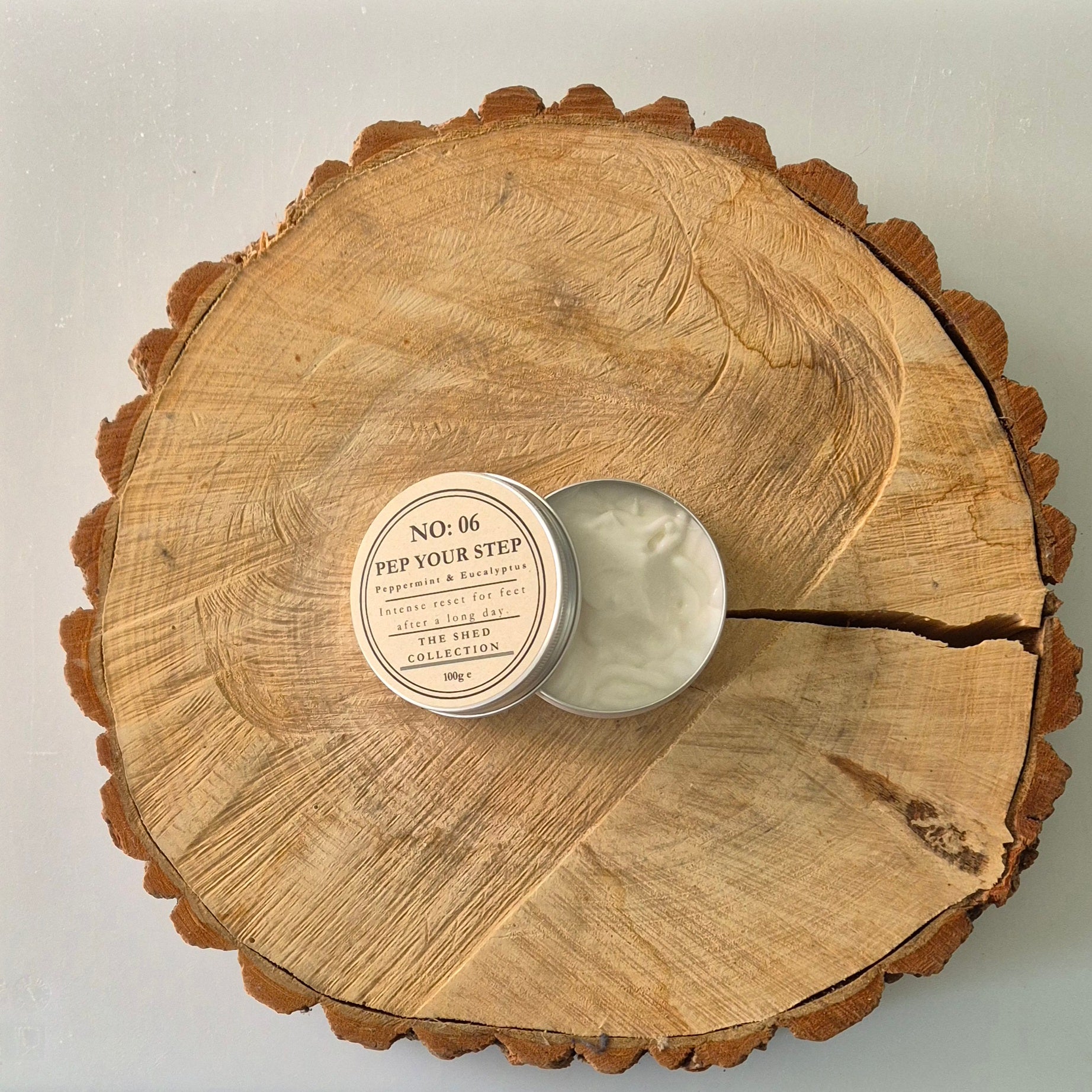 Open tin labelled 'Pep Your Step' Peppermint & Eucalyptus Foot Cream on a log slice