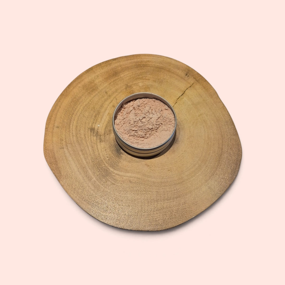 Pink clay powder in an aluminium tin on a log slice