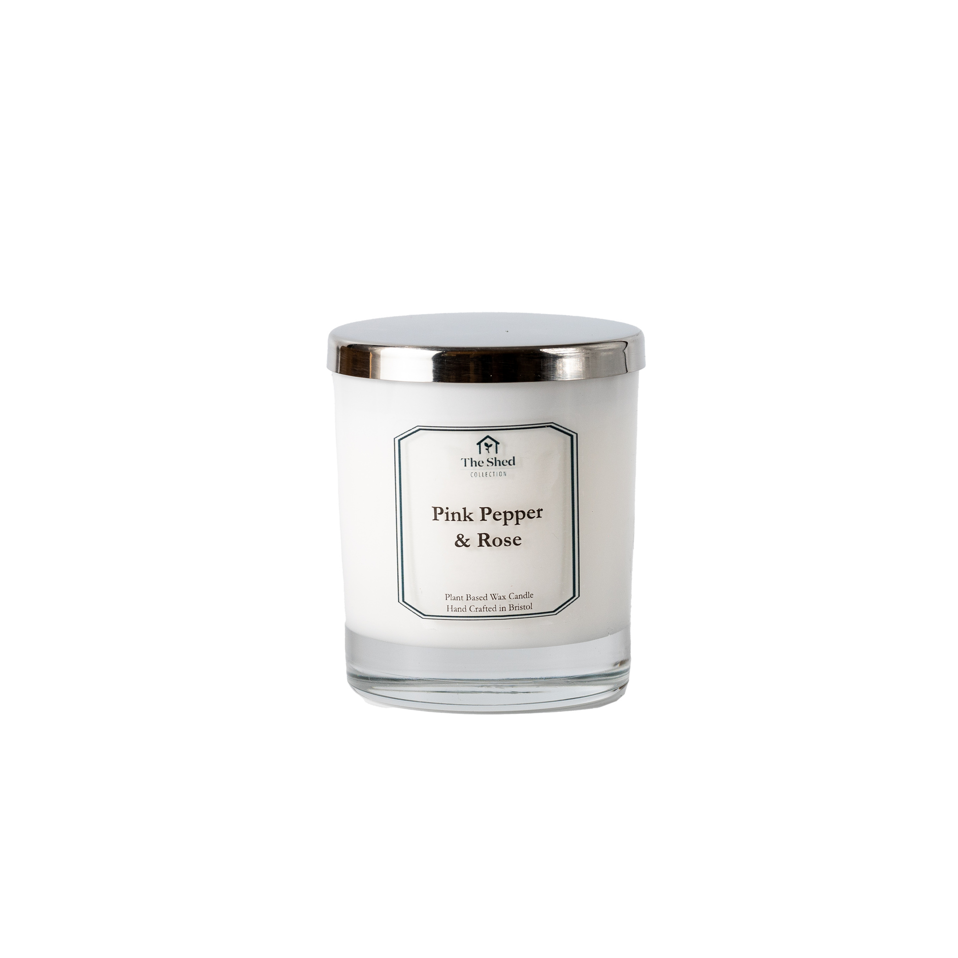 A white wax candle in a clear glass jar with a shiny silver metal lid, featuring a white label with black text that reads 'The Shel Pink Pepper & Rose'.