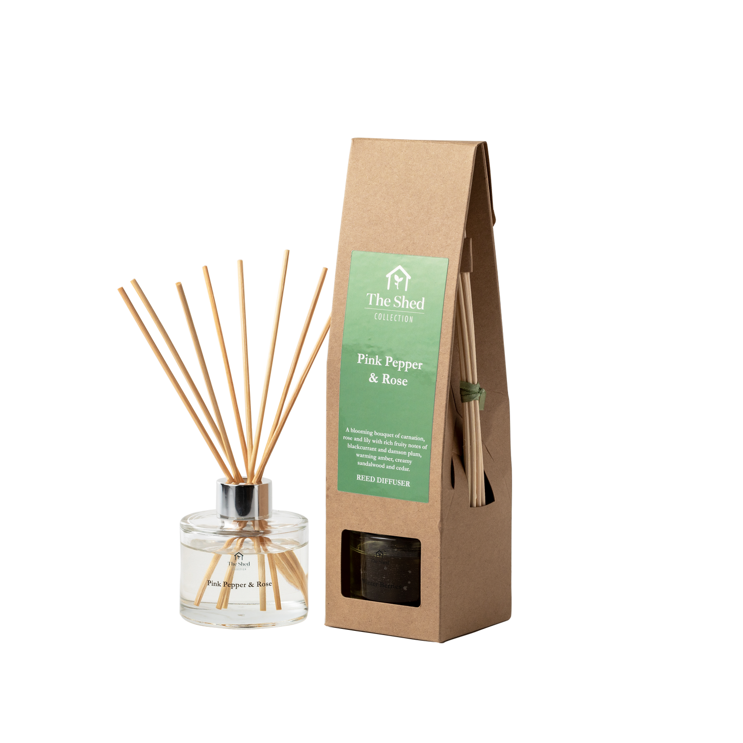 A reed diffuser bottle with natural reeds next to its brown kraft paper packaging bag. The box features a green label that reads 'The Shed Collection' and 'Pink Pepper & Rose'.