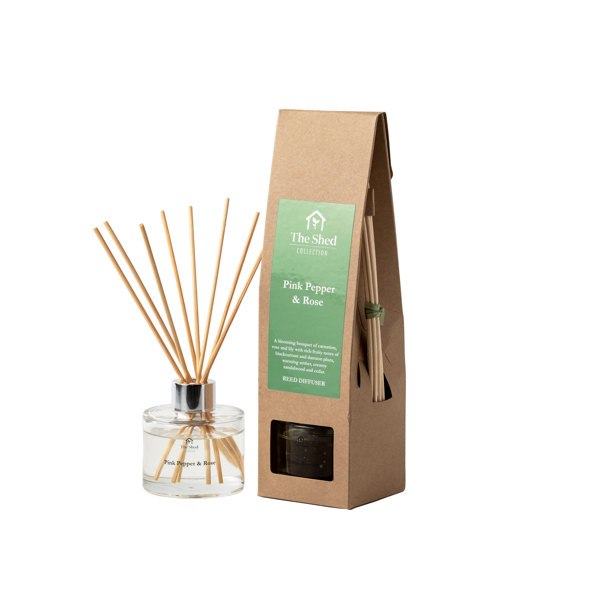 A reed diffuser bottle with natural reeds next to its brown kraft paper packaging bag. The box features a green label that reads 'The Shed Collection' and 'Pink Pepper & Rose'.