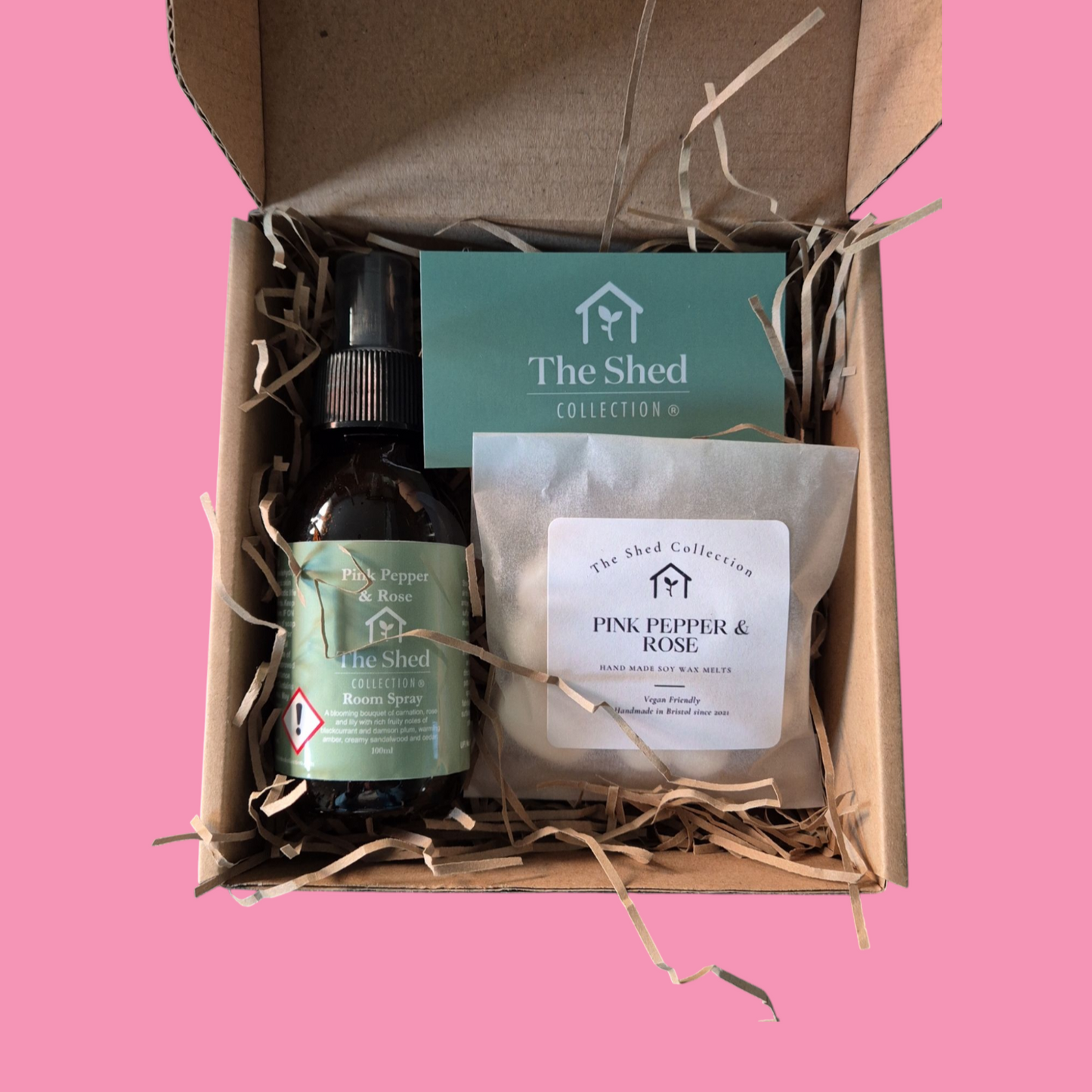 A gift set from The Shed Collection, including a wax melt and a room spray in a cardboard box with straw bedding, labeled with different fragrance names.