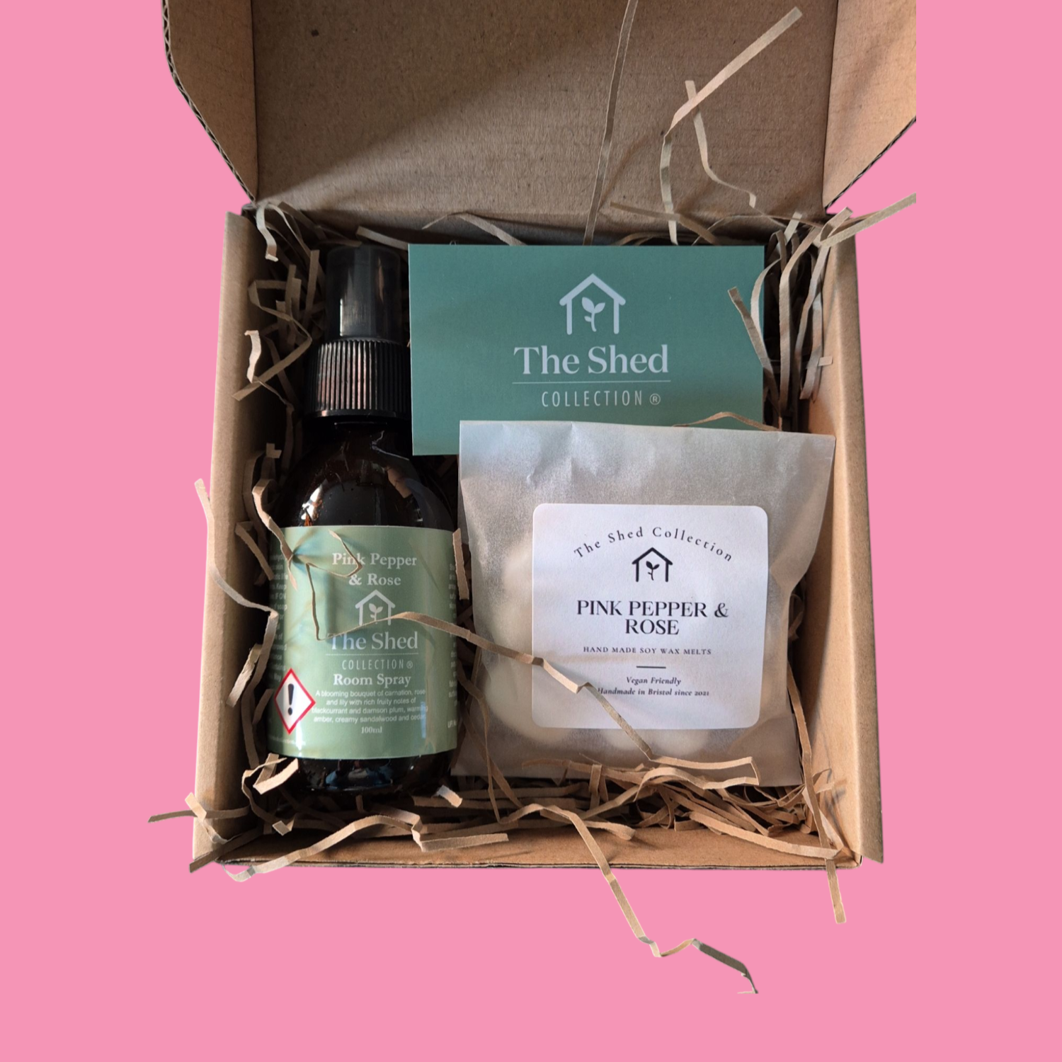 A gift set from The Shed Collection, including a wax melt and a room spray in a cardboard box with straw bedding, labeled with different fragrance names.