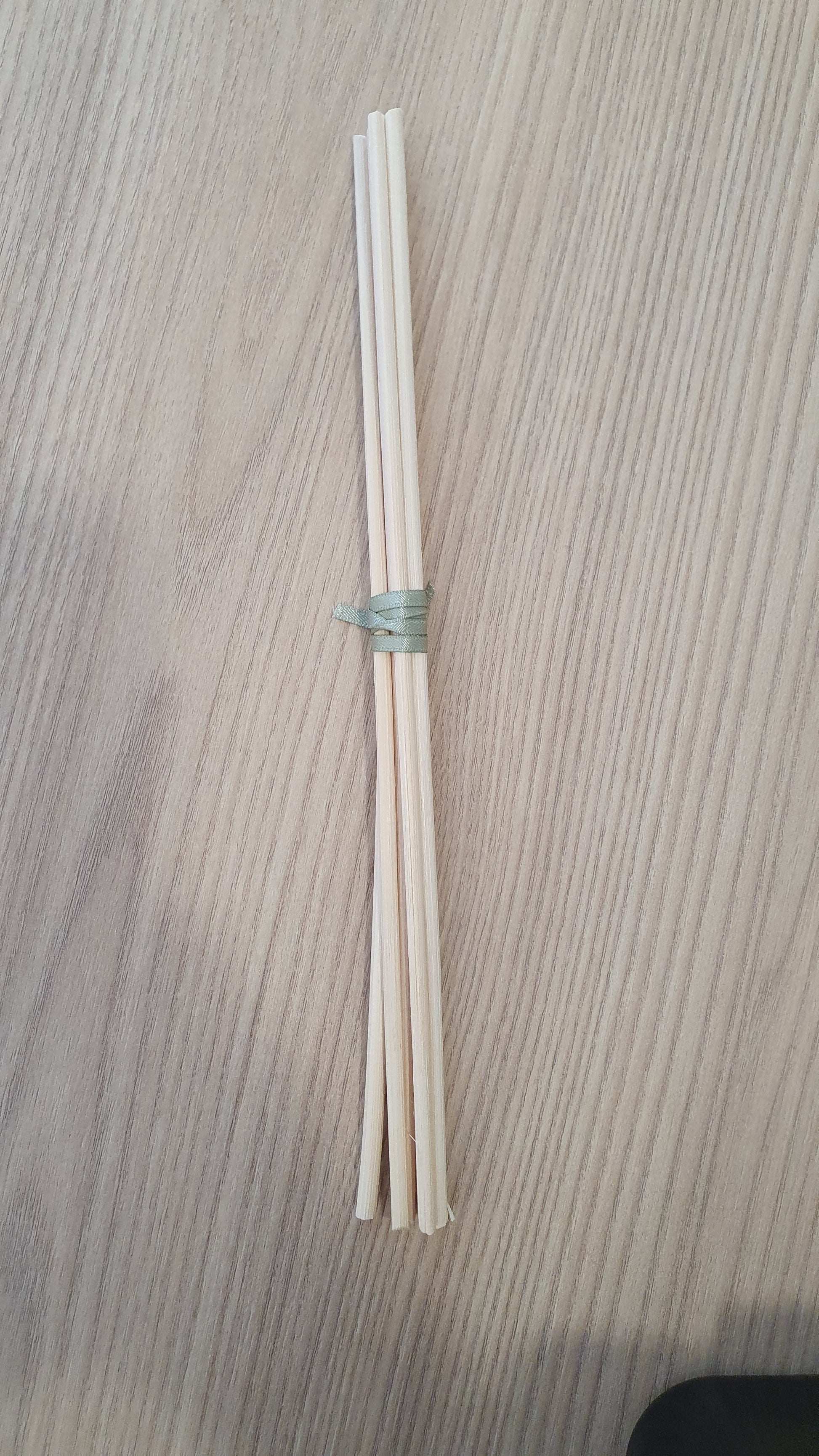 A set of six white diffuser reeds tied together, placed on a textured surface.