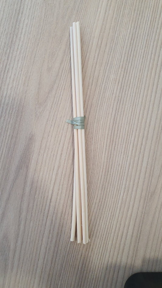 A set of six white diffuser reeds tied together, placed on a textured surface.