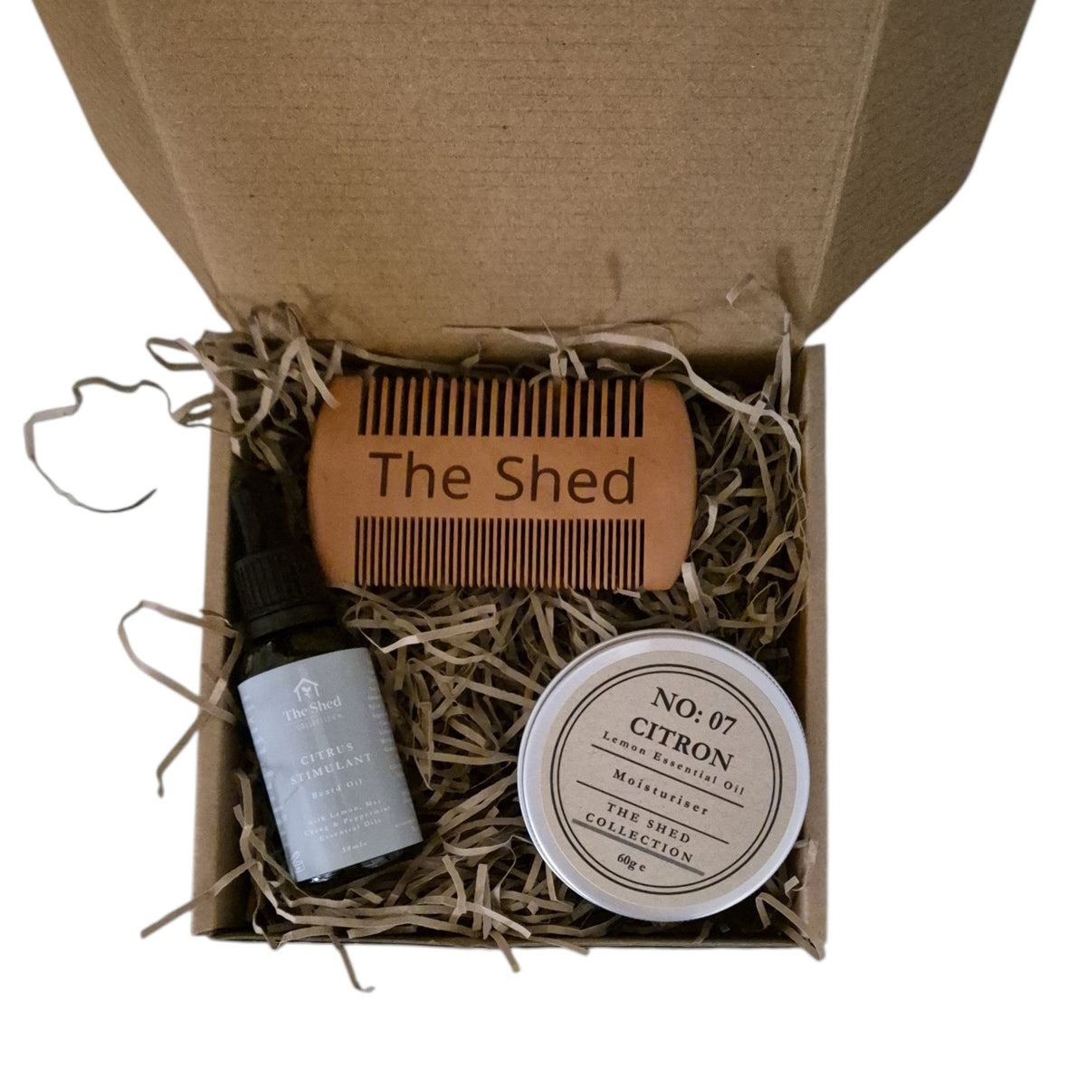 A curated beard care gift set from The Shed Collection, in a brown cardboard gift box, a small dropper bottle of beard oil, a tin of moisturiser and a beard comb.