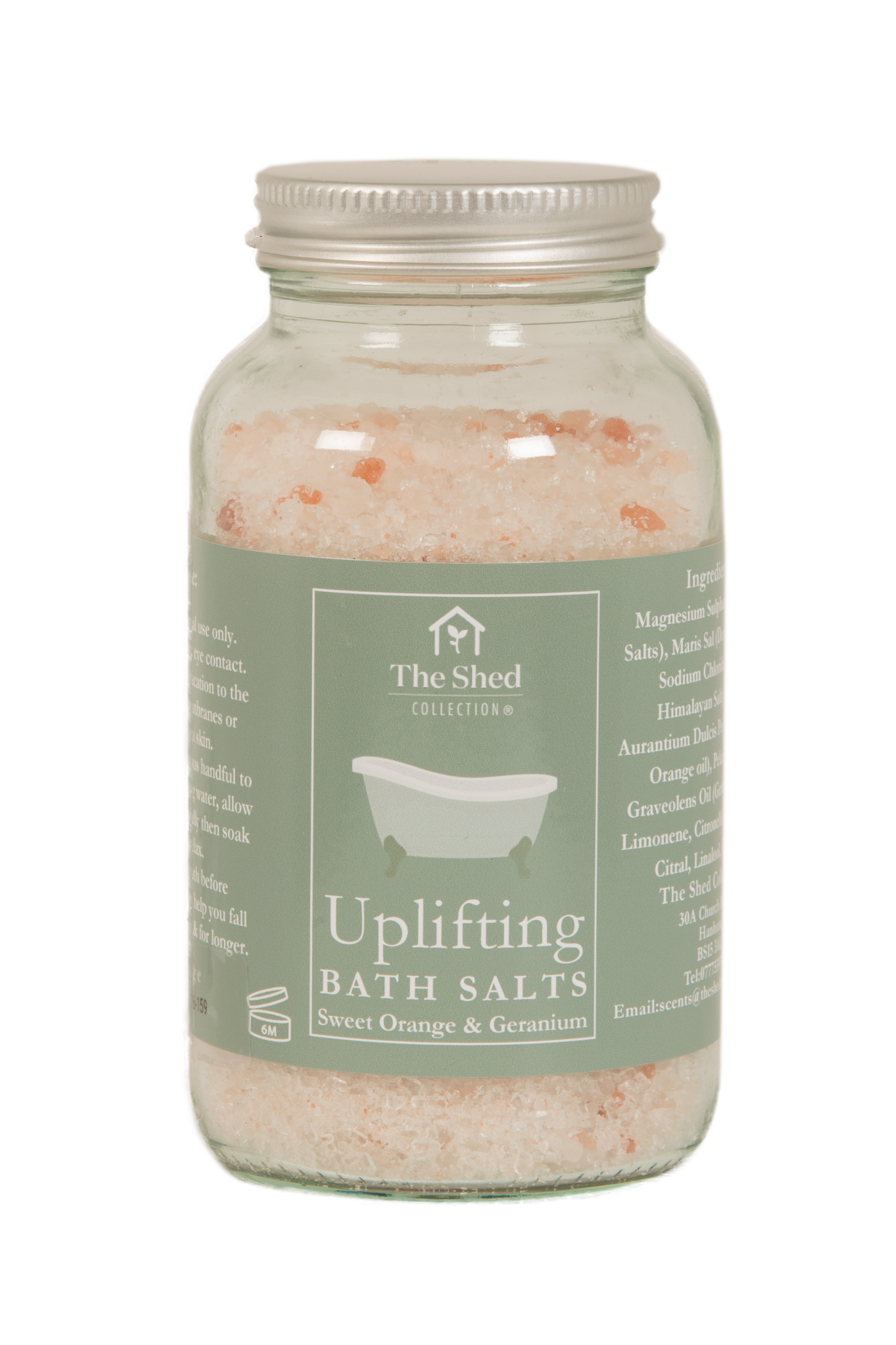 A glass jar of 'Uplifting Bath Salts' by The Shed Collection, filled with pink and orange crystalline bath salts, featuring a sage green label and a silver metal lid.