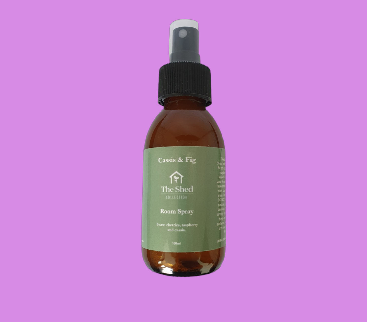 Picture shows a vegan friendly Cassis & Fig room spray from The Shed Collection in a brown glass bottle with black spray lid against a pinky purple background.